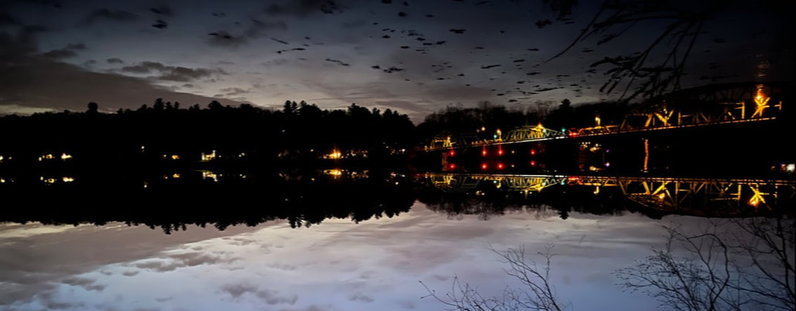 The Rocks Village Bridge illuminated at twilight, reflecting in the Merrimack River